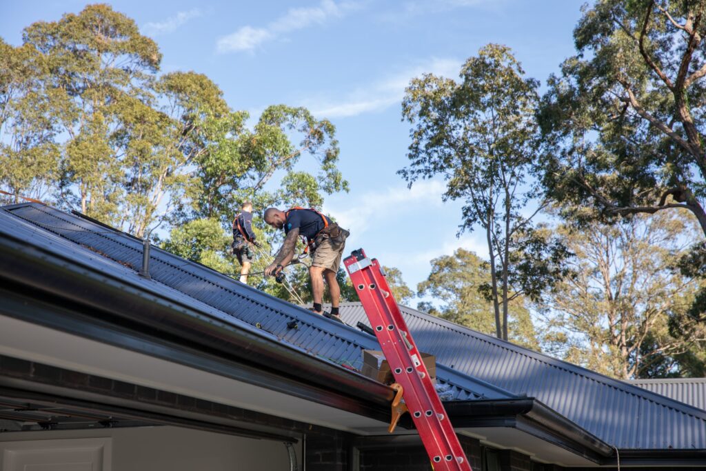 An installer crossing a metal roof in a safety harness, the Central West & Riverina