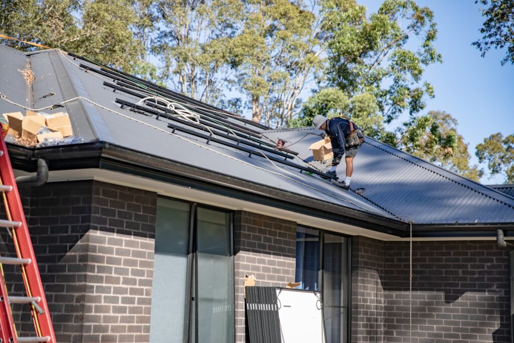 An installer at the roof edge beside an extension ladder, the Hunter Valley