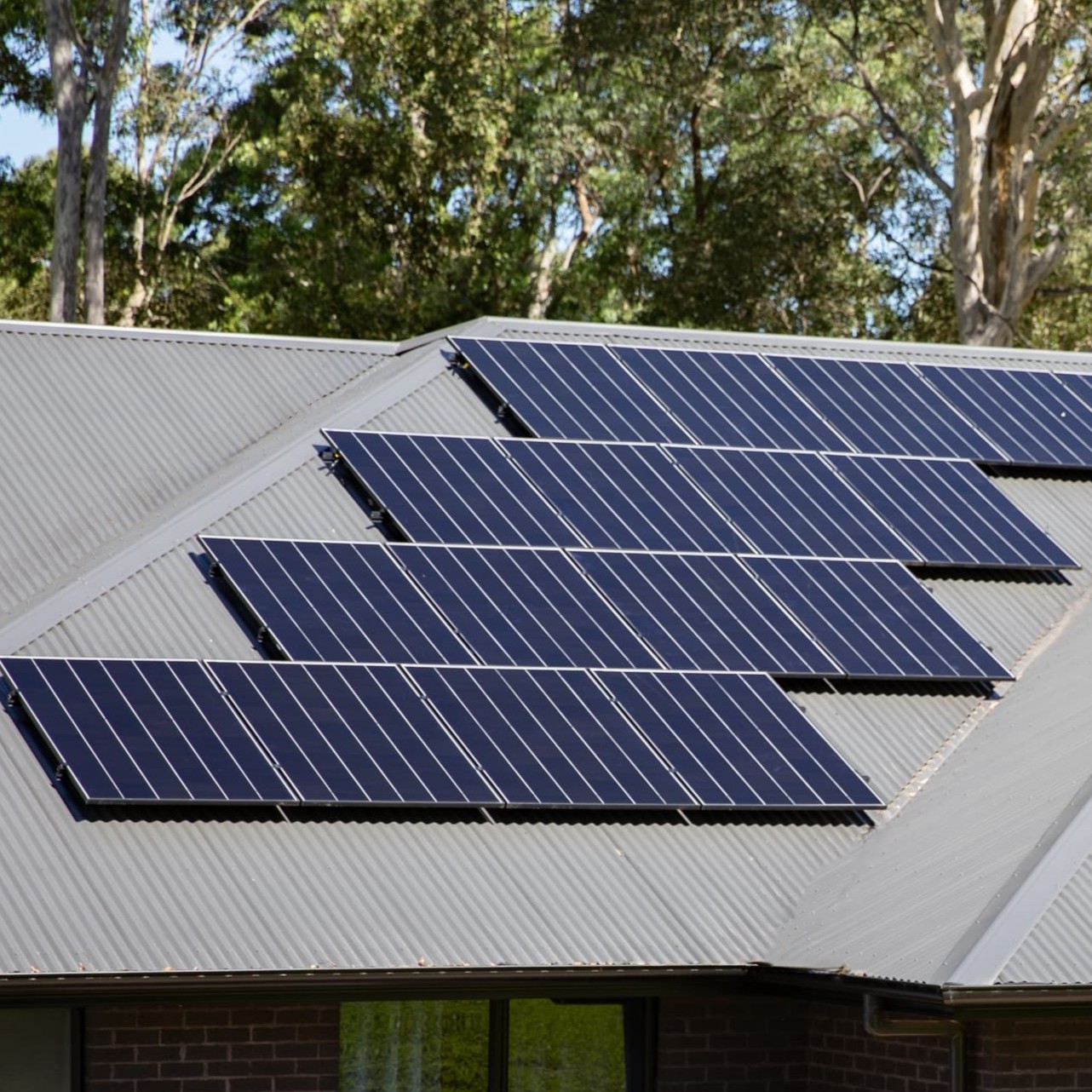 Two rows of solar panels on the corrugated roof of a brick house