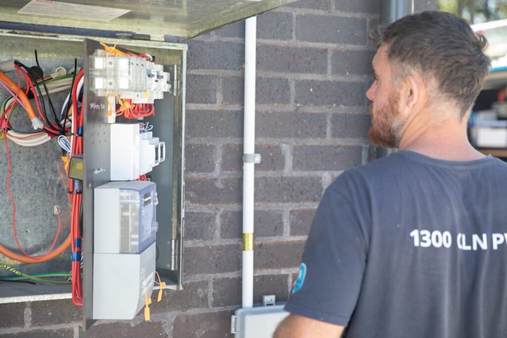 An installer checking an open switchboard on an exterior wall, Canberra & the ACT