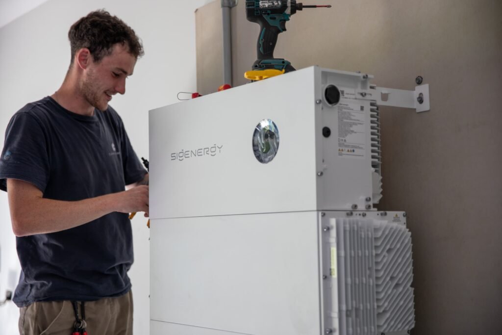 An installer using a drill above a battery and inverter unit