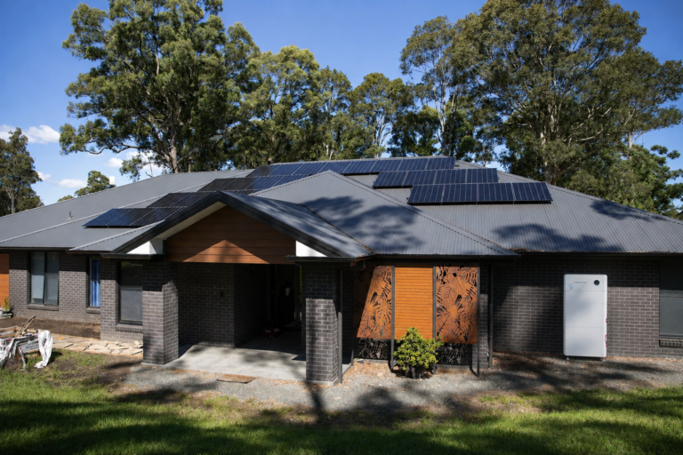 A single-storey brick home with solar panels on the roof and a battery on the wall