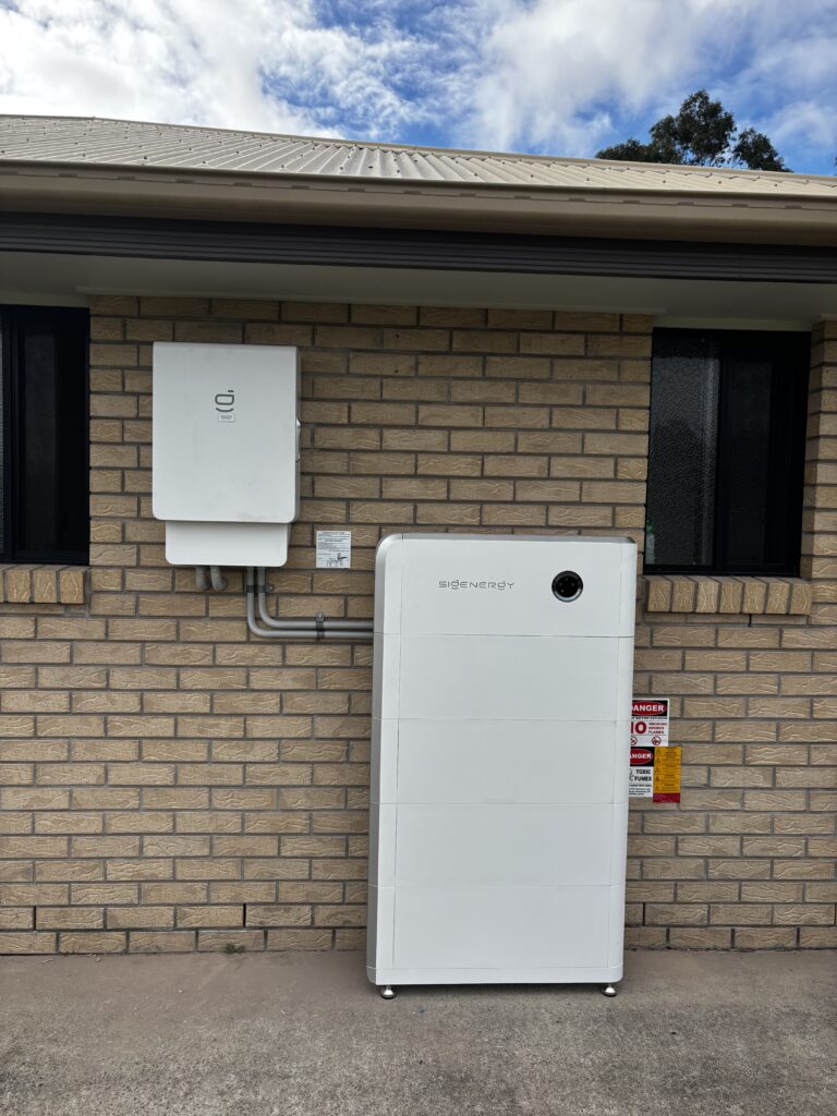 An inverter and a floor-standing battery installed against a brick house wall