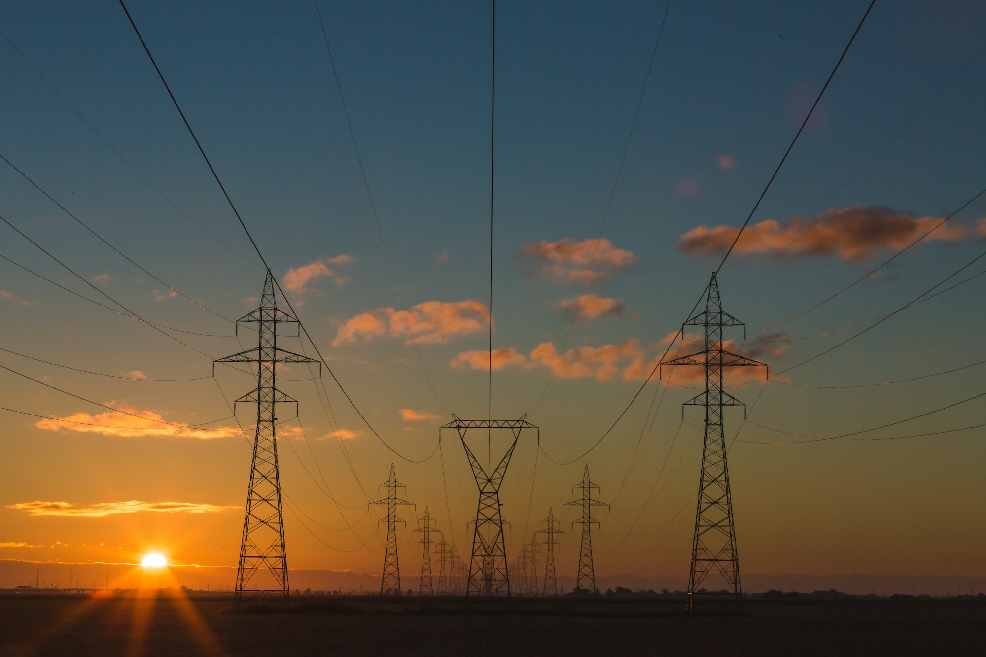 High voltage transmission towers silhouetted against an evening sunset